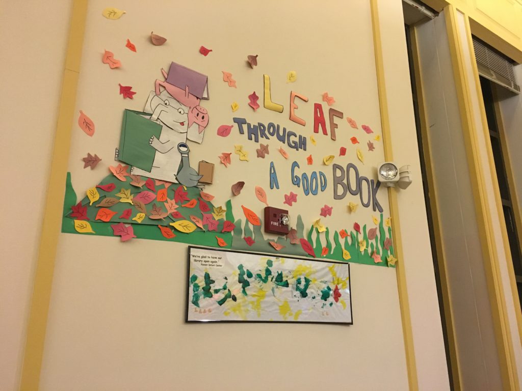 Paper wall decoration featuring falling leaves surrounding an elephant, a pig, and a goose who are all reading, with the text "leaf through a good book"