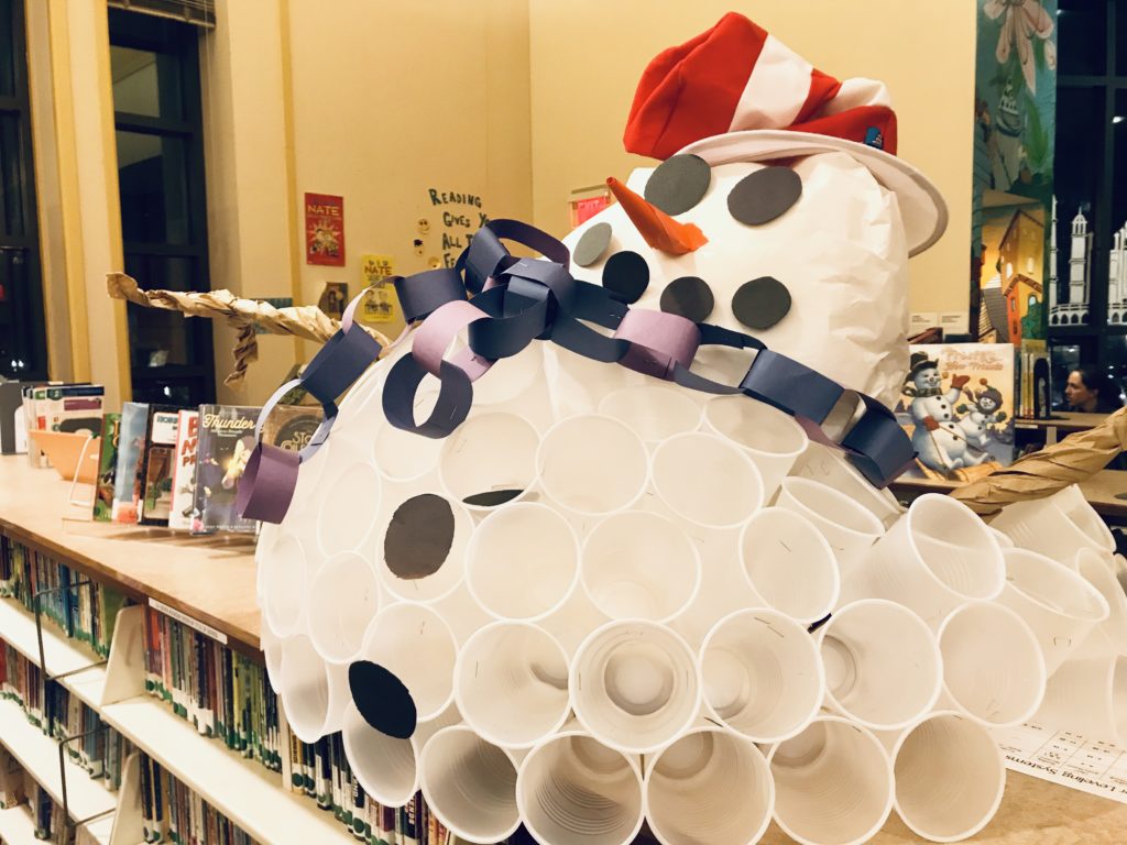 A round snowman made of plastic cups, wearing a paper chain scarf and a striped hat