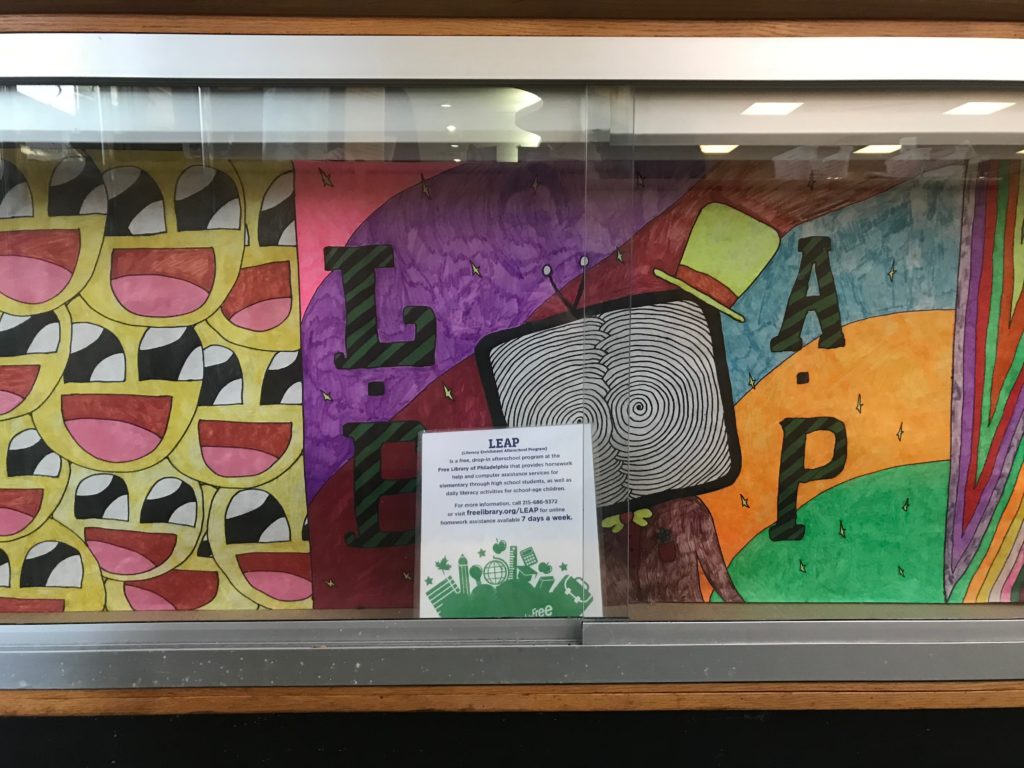 Display case with vibrant artwork including the word "LEAP", and a sign about the LEAP program in the foreground