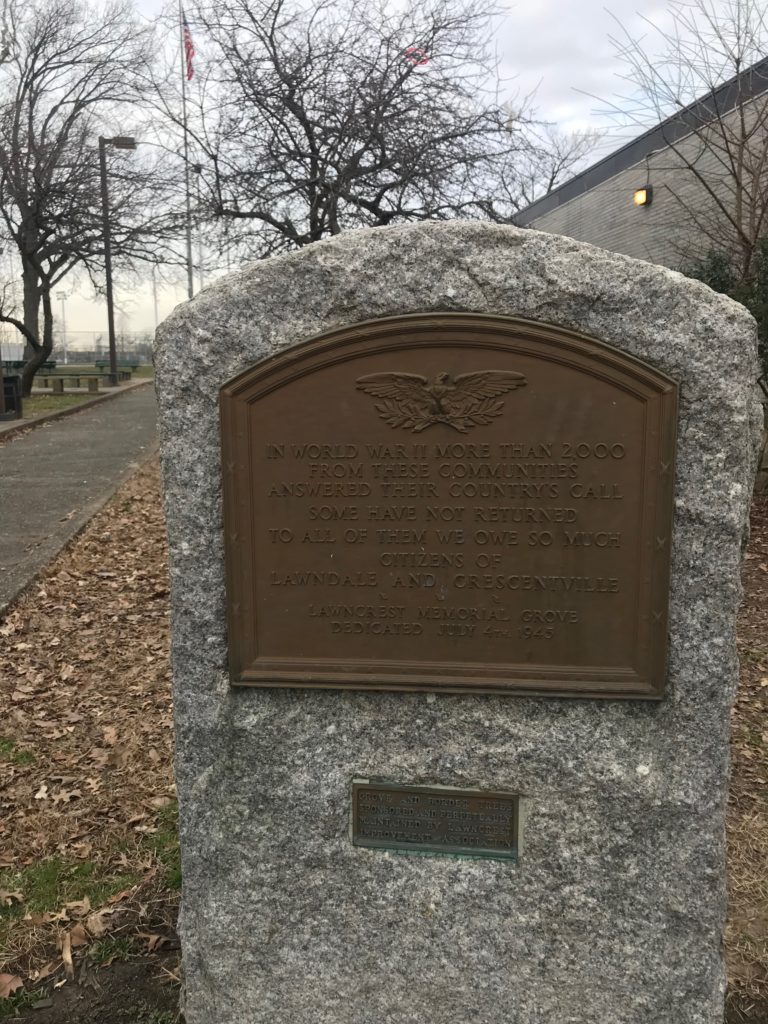 Stone memorial with embedded bronze plaque in the foreground with bare winter trees in the background